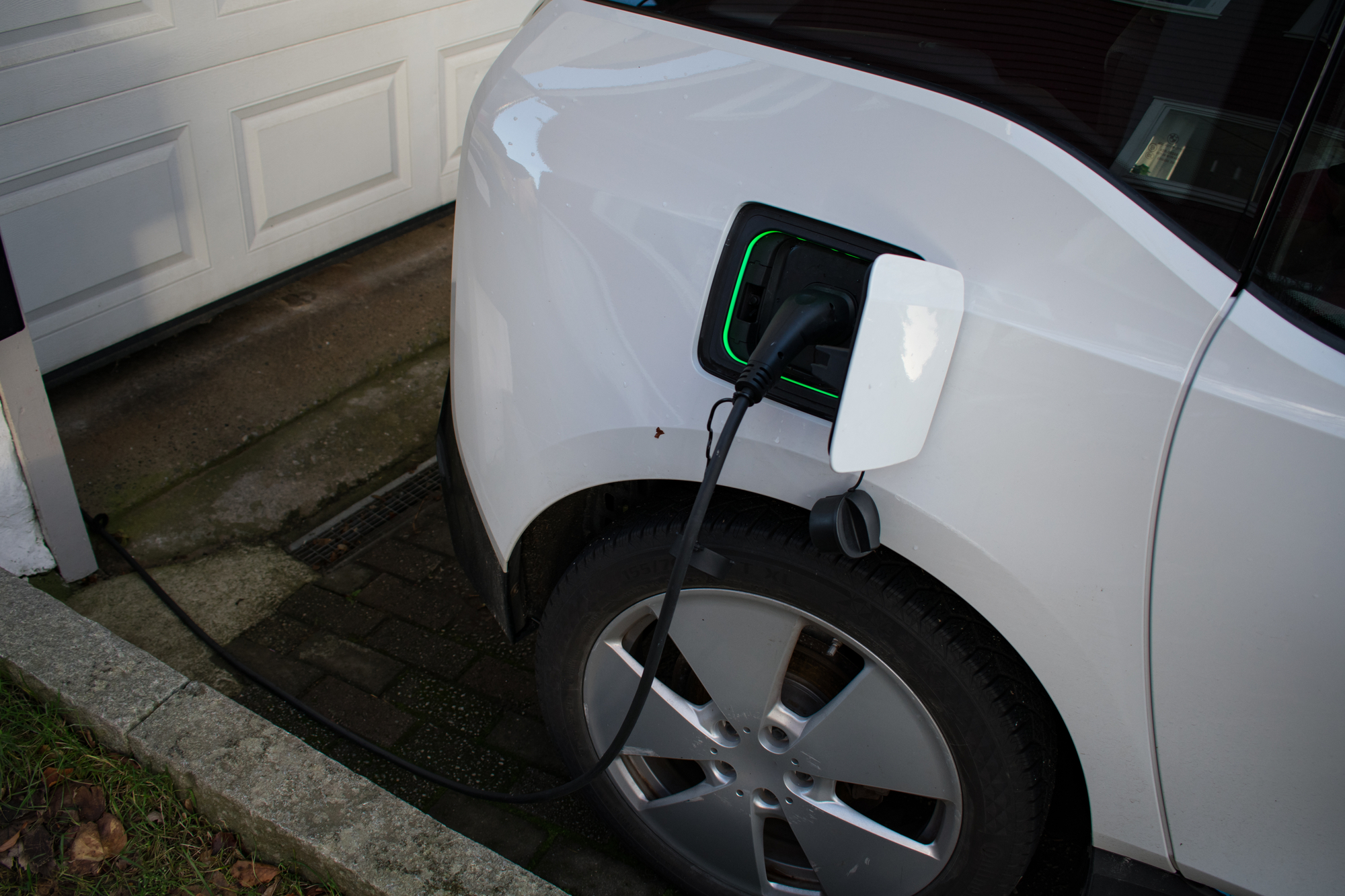 White electric vehicle being charged at home with a green illuminated charging port indicating ongoing EV home charging installation in the DFW area