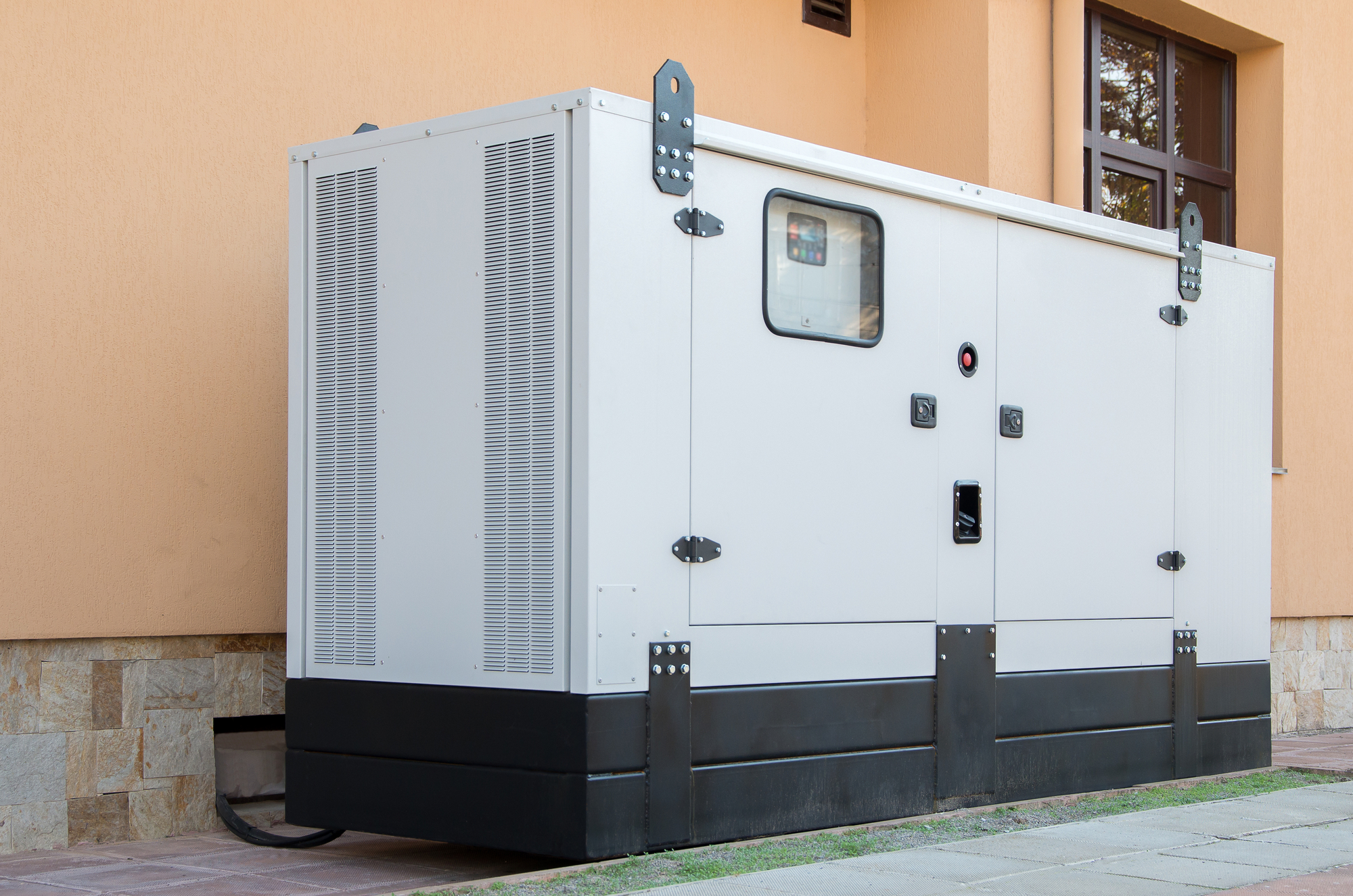 A large, stationary backup power generator is installed outside a building, with ventilation grills and a small window