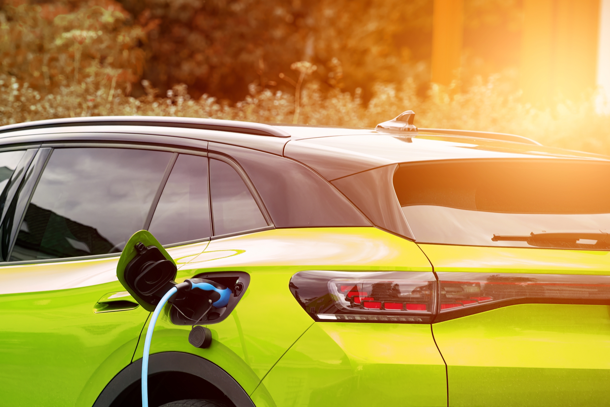 An electric vehicle being charged at home during sunset, illustrating eco-friendly transportation options